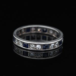 May include: A silver band ring with a row of alternating blue sapphires and white diamonds.