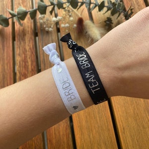 Op de afbeelding: Twee witte elastiekjes voor haar met zilveren glitterhartjes en de woorden "Bride" en "Team Bride" erop gedrukt.