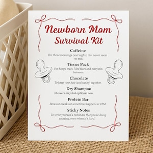 May include: A white card with the text "Newborn Mom Survival Kit" in red script. The card lists items like caffeine, tissue pack, chocolate, dry shampoo, protein bar, and sticky notes, with pacifier illustrations.
