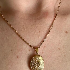 K&ouml;nnte beinhalten: Goldfarbene ovale Medaillon-Anh&auml;nger-Halskette. Das Medaillon hat ein florales Design und h&auml;ngt an einer zarten Kette. Ein klassisches Schmuckst&uuml;ck.