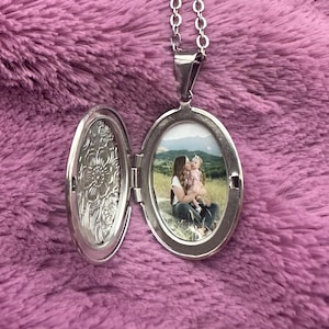 May include: Silver locket necklace with a photo of a woman and a child in a field. The locket has a floral design on the back.
