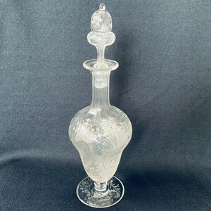 May include: A clear glass decanter with a stopper. The decanter has a textured, floral design and a round base.