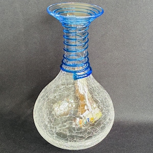 May include: A clear glass vase with a bulbous body and a blue spiral neck. The vase has a crackle finish, and the neck is adorned with blue spiral detailing. The vase is likely for decorative purposes.