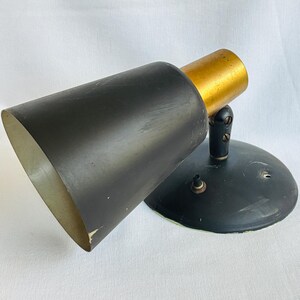 May include: A vintage black and gold wall-mounted lamp. The lamp features a black, cone-shaped shade and a gold-colored cylindrical section. The base is a rounded, black disc. The lamp is designed to be mounted on a wall.