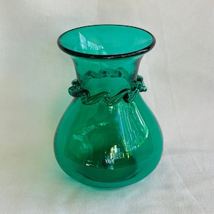May include: A teal green glass vase with a decorative, twisted glass rim.