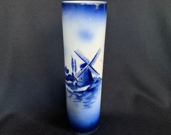 May include: A blue and white ceramic vase with a windmill scene painted on the side. The vase is cylindrical in shape and has a smooth, glossy finish.