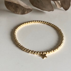 May include: Gold beaded bracelet with a small star charm. The bracelet features small, round gold beads strung together, forming a delicate and elegant accessory. The star charm adds a touch of whimsy to the design. This bracelet is a stylish piece of jewelry.