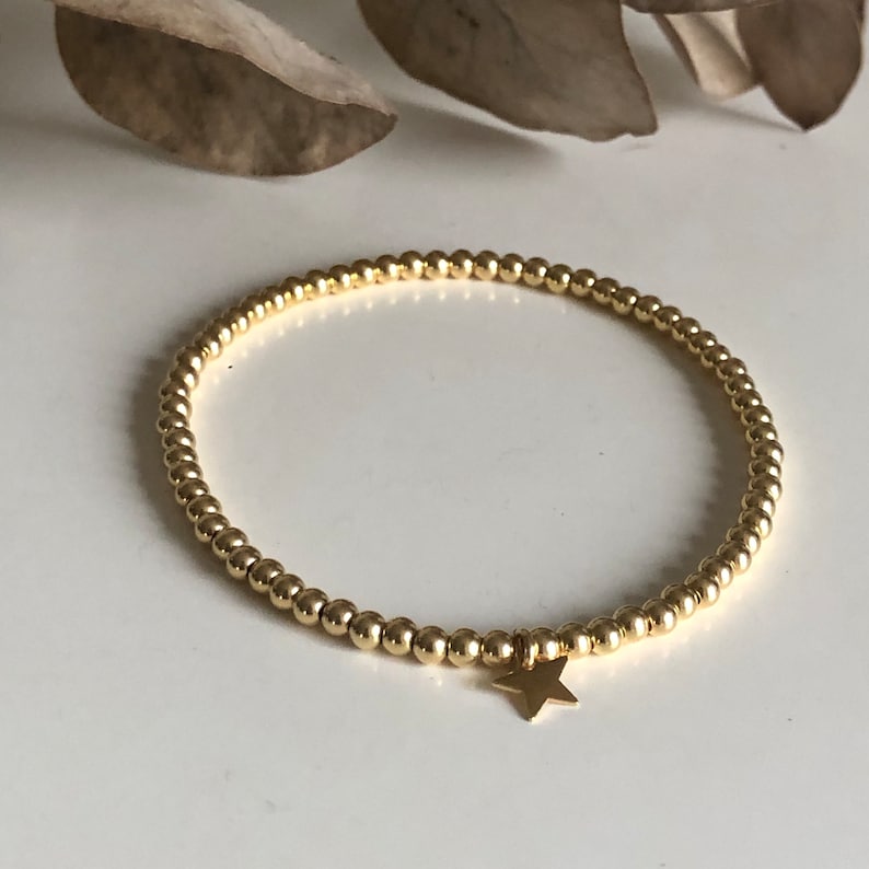 May include: Gold beaded bracelet with a small star charm. The bracelet features small, round gold beads strung together, forming a delicate and elegant accessory. The star charm adds a touch of whimsy to the design. This bracelet is a stylish piece of jewelry.