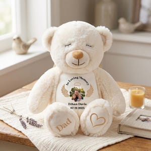 Könnte beinhalten: Cremefarbener Teddybär mit geschlossenen Augen, mit Gedenkdesign. Der Bär hat ein Foto, Engelsflügel und den Text "In Loving Memory" und "Ethan Davis 07/21/2025." Der Fuß des Bären hat das Wort "Dad" und ein Herz.