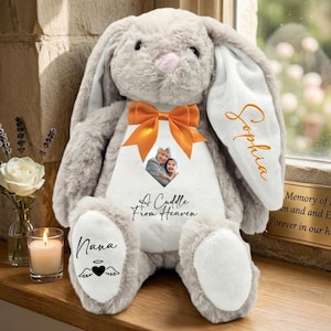 May include: A grey plush bunny with an orange bow and a photo. The bunny has the name "Sophia" on one ear and the words "A Cuddle From Heaven" on its chest. The word "Nana" is on one foot.