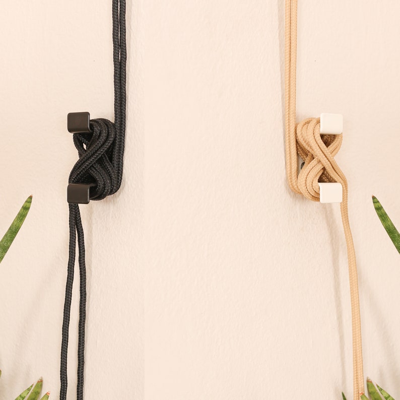 May include: Two hanging plant holders, one black and one beige, with a simple knot design and white plastic clips.
