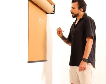 May include: A person writing on a brown paper roll mounted on a wall with a black metal frame. The roll is labeled "home" and has a wooden top rail.