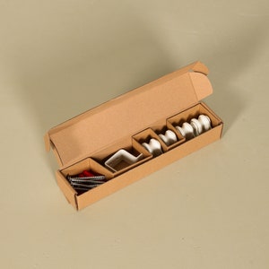 May include: A cardboard box with a variety of white ceramic curtain rod holders and red screws. The box is open and the contents are visible.