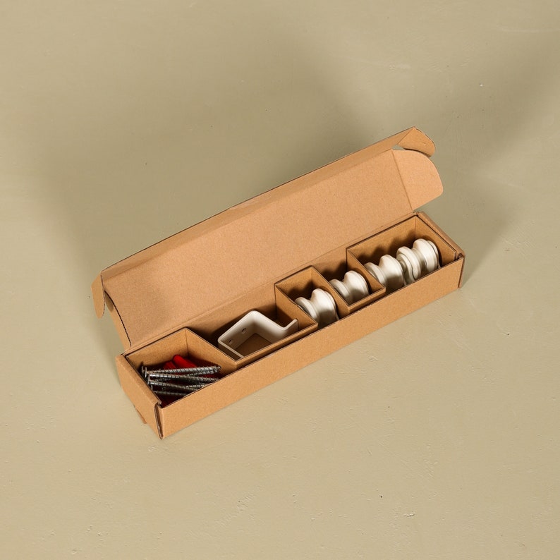 May include: A cardboard box with a variety of white ceramic curtain rod holders and red screws. The box is open and the contents are visible.