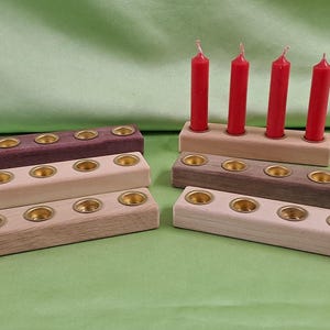 Könnte beinhalten: Fünf Kerzenhalter aus Holz mit Messing-Kerzenbechern. Die Halter sind in verschiedenen Holztönen, darunter helles Holz, dunkles Holz und violettes Holz. Vier rote Kerzen befinden sich im oberen Halter.