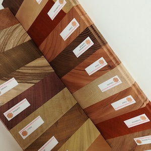 Könnte beinhalten: Eine Sammlung von 15 Holzproben, jede mit der Holzart und der Website des Holzlieferanten beschriftet. Die Holzproben sind versetzt angeordnet, wobei die Etiketten zum Betrachter zeigen. Die Holzarten umfassen Zebrano, Amaranth, Limba, Lati, Schwarzer Holunder, Doussie, Ebiara, Schotendom, Kirschbaum, Hainbuche, Korallenholz und mehr.