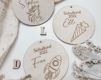 May include: Three wooden ornaments with the text "Schulkind 2022" and a child's name. The first ornament features a horse, the second a party hat, and the third a rocket.