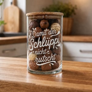 Könnte beinhalten: Ein zylindrisches Glasgefäß mit Holzdeckel, gefüllt mit verschiedenen Milch- und Zartbitterschokoladen. Auf der Vorderseite befindet sich der weiße, geschwungene Schriftzug: Damit der Schlüppi nicht rutscht, verziert mit kleinen weißen Schnörkeln.