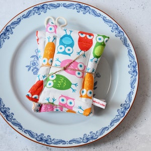 Könnte beinhalten: Zwei weiße Stoff-Topflappen mit einem bunten Eulen-Druck. Die Topflappen sind mit Schnur zusammengebunden und haben ein Etikett mit der Aufschrift "labohatte".
