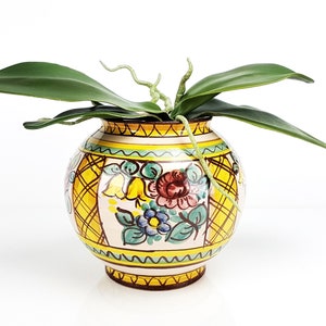 Peut inclure: Un pot en céramique jaune, blanc et vert avec un motif floral. Le pot a une forme ronde et une large ouverture. Une plante d'orchidée verte est dans le pot.