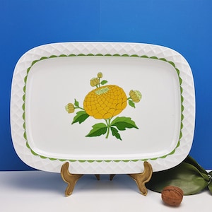 Könnte beinhalten: Weißes rechteckiges Serviertablett mit einem grünen und weißen gewellten Rand. In der Mitte des Tabletts befindet sich eine gelbe Blume mit grünen Blättern und Stielen.