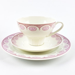 May include: A white teacup and saucer set with a pink and red floral pattern. The cup and saucer have a scalloped edge.
