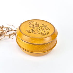 Peut inclure: Une boîte ronde en bois avec un motif floral. La boîte est en bois clair et possède un couvercle qui s'emboîte parfaitement sur le dessus. Le motif floral est gravé dans le bois et représente un bouquet de roses.