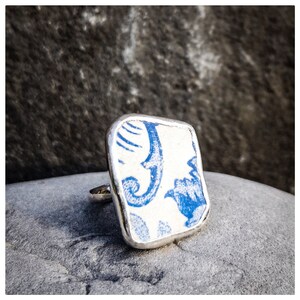 May include: A silver ring with a square blue and white patterned ceramic top.
