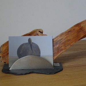 Peut inclure: Un présentoir composé d'une base en branche de bois naturel, d'un socle en ardoise noire et d'un support en métal brossé semi-circulaire. Une carte rectangulaire avec un graphique gris d'un objet arrondi est maintenue dans la fente.
