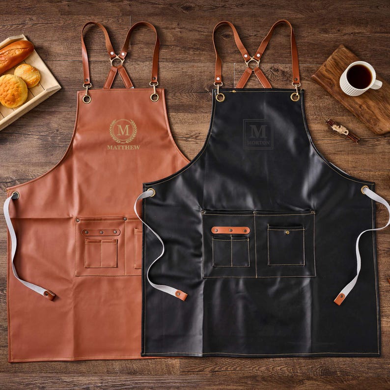 May include: Two leather aprons with adjustable straps. One apron is brown with the name "Matthew" and the other is black with the name "Moritz".