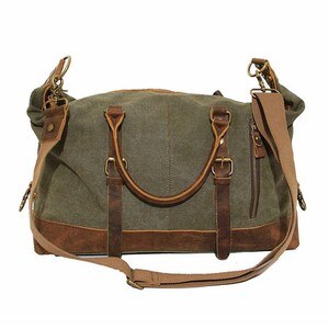 May include: An olive green canvas duffel bag featuring brown leather trim, two top handles with buckle accents, a side zippered pocket, and a detachable beige fabric shoulder strap with metal hardware clips attached to the sides of the bag.