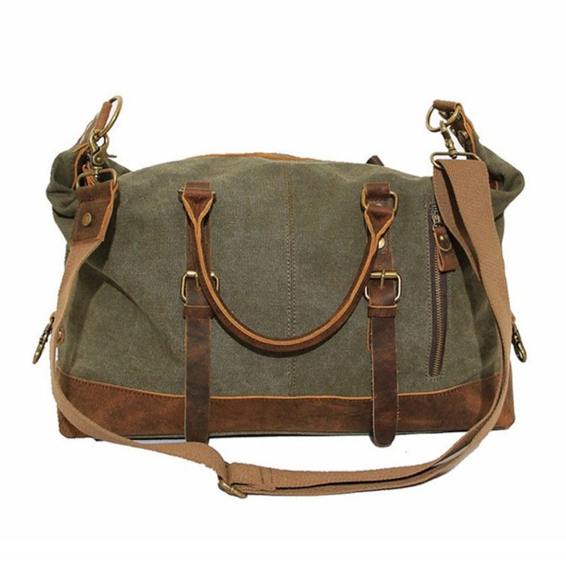 May include: An olive green canvas duffel bag featuring brown leather trim, two top handles with buckle accents, a side zippered pocket, and a detachable beige fabric shoulder strap with metal hardware clips attached to the sides of the bag.