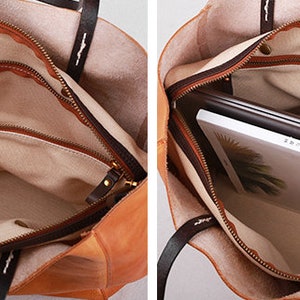 May include: Inside view of a brown leather tote bag with a beige fabric lining. The bag has two zipped compartments and a large open space. The bag is shown with a laptop and a book inside.