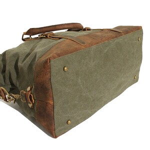May include: A duffel bag constructed from olive green canvas and brown leather trim. The bag features a rectangular base with four brass-toned metal feet, a top handle, and side attachment points for a shoulder strap with brass-toned hardware.