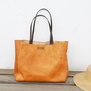 May include: A tan leather tote bag with brown leather handles. The bag has a monogrammed "HSK" on the front.