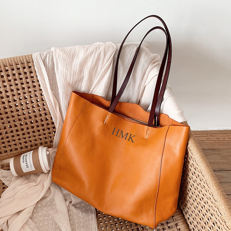 May include: A large, orange leather tote bag with brown leather handles. The bag has a stitched design and the initials "HMK" are embossed on the front.