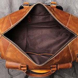 May include: A brown leather duffel bag with a zippered opening and two handles. The bag is open and the inside is lined with brown fabric.