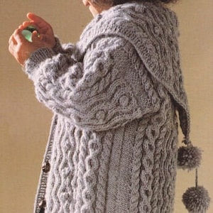 May include: A gray knitted cardigan with a hood and a cable knit pattern. The cardigan has a button closure and is decorated with pom-poms.