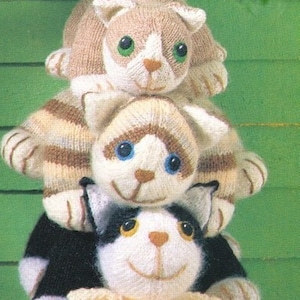May include: Four knitted cat toys stacked on top of each other. The cats are different colours and have different patterns. The bottom cat is orange and white, the next cat is black and white, the next cat is brown and white, and the top cat is beige and white.