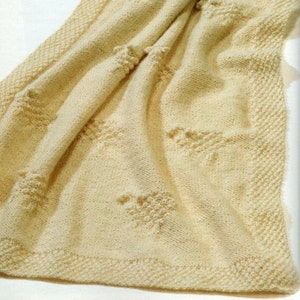May include: A cream-colored knitted baby blanket with a textured pattern. The blanket is folded in half and has a border around the edges.