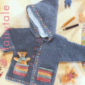 May include: A blue knitted baby cardigan with a hood, featuring a teddy bear applique and colourful striped pockets. The cardigan has a button fastening and is decorated with embroidered details.