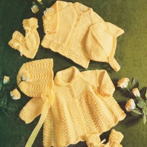 May include: A set of knitted baby clothes in a pale yellow color. The set includes a cardigan, a bonnet, a dress, and booties.