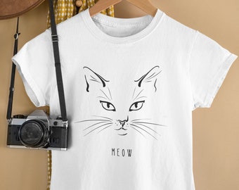 Può includere: Maglietta bianca con un disegno a linea nera di un viso di gatto e la parola "MEOW" stampata sotto.