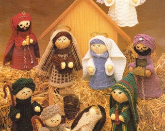 May include: A knitted nativity scene with figures of Mary, Joseph, baby Jesus, an angel, three wise men, and two shepherds. The figures are all dressed in traditional clothing and are arranged in a manger setting.