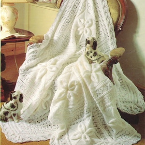 May include: A white crocheted blanket with a delicate floral pattern. The blanket is draped over a wooden chair with a white cushion. Two small porcelain dogs are sitting on the blanket.