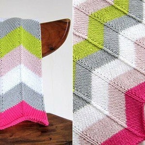 May include: A knitted baby blanket with a chevron pattern in shades of pink, white, gray, and green. The blanket has a scalloped edge.