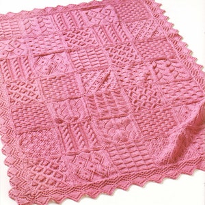 May include: A pink knitted blanket featuring a range of different stitch patterns. The blanket has a scalloped edge.