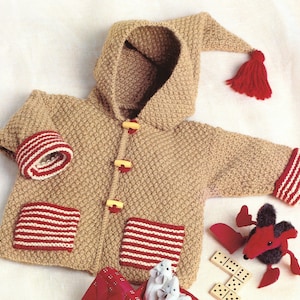 May include: A tan knitted hooded jacket with red and white striped trim on the cuffs and pockets. The jacket has a pointed hood with a red tassel and yellow buttons.