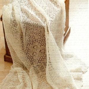 May include: A delicate white lace shawl with a delicate floral pattern. The shawl is draped over a wooden stool.