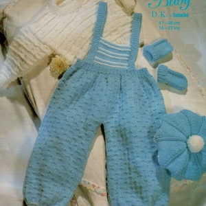 May include: A knitted baby outfit set in blue and white. The set includes a hat, booties, mittens, and a pair of dungarees with a white top. The dungarees have a white stripe detail. The set is made with D.K. Cashmere yarn and is for a baby 16-22 inches (41-56 cm).